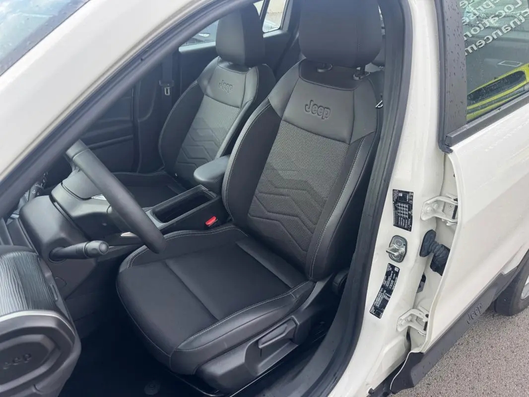 Vue intérieure côté conducteur du Jeep Avenger blanc 2025, mettant en valeur les sièges noirs avec logo Jeep embossé.