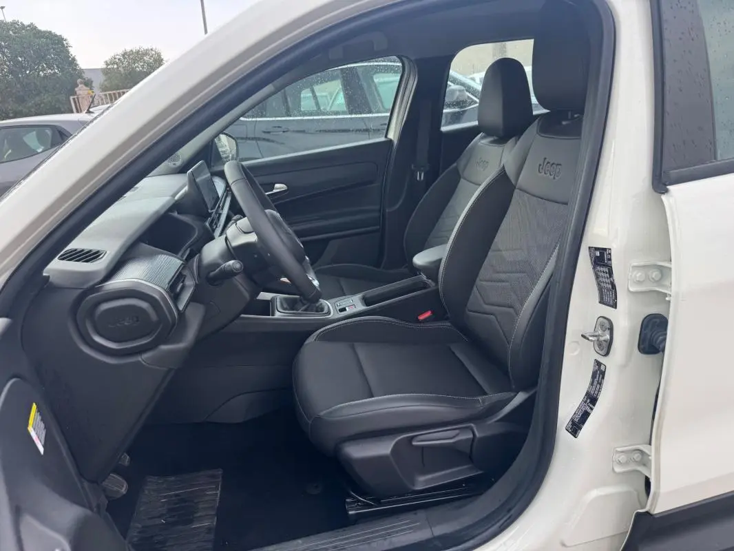 Intérieur avant droit du Jeep Avenger blanc 2025, sièges noirs avec logo Jeep brodé, volant et console centrale visibles.