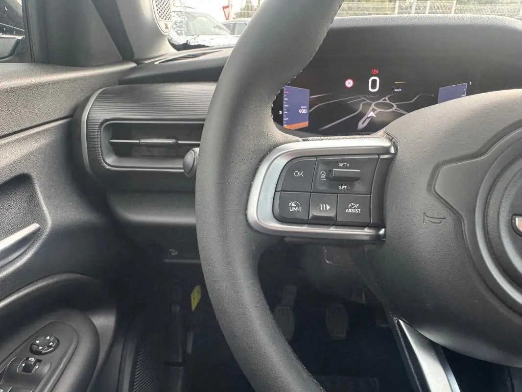 Vue intérieure centrée sur le volant et le tableau de bord numérique du Jeep Avenger blanc, avec commandes au volant visibles.