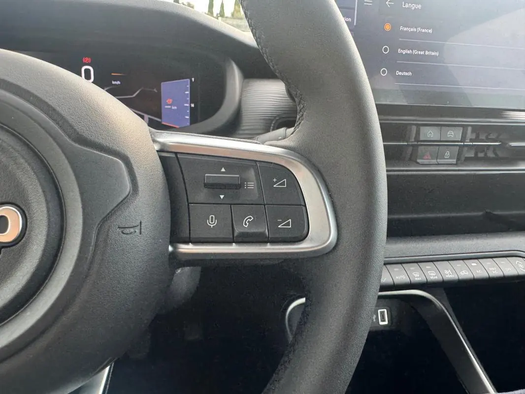 Vue rapprochée du volant à droite avec commandes intégrées et partie du tableau de bord numérique du Jeep Avenger blanc 2025.