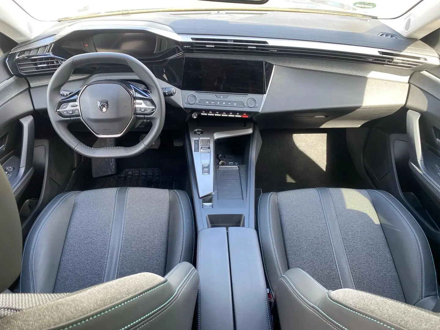 Vue intérieure avant de la Peugeot 308 2025 gris, montrant le volant multifonction, écran tactile et console centrale moderne.