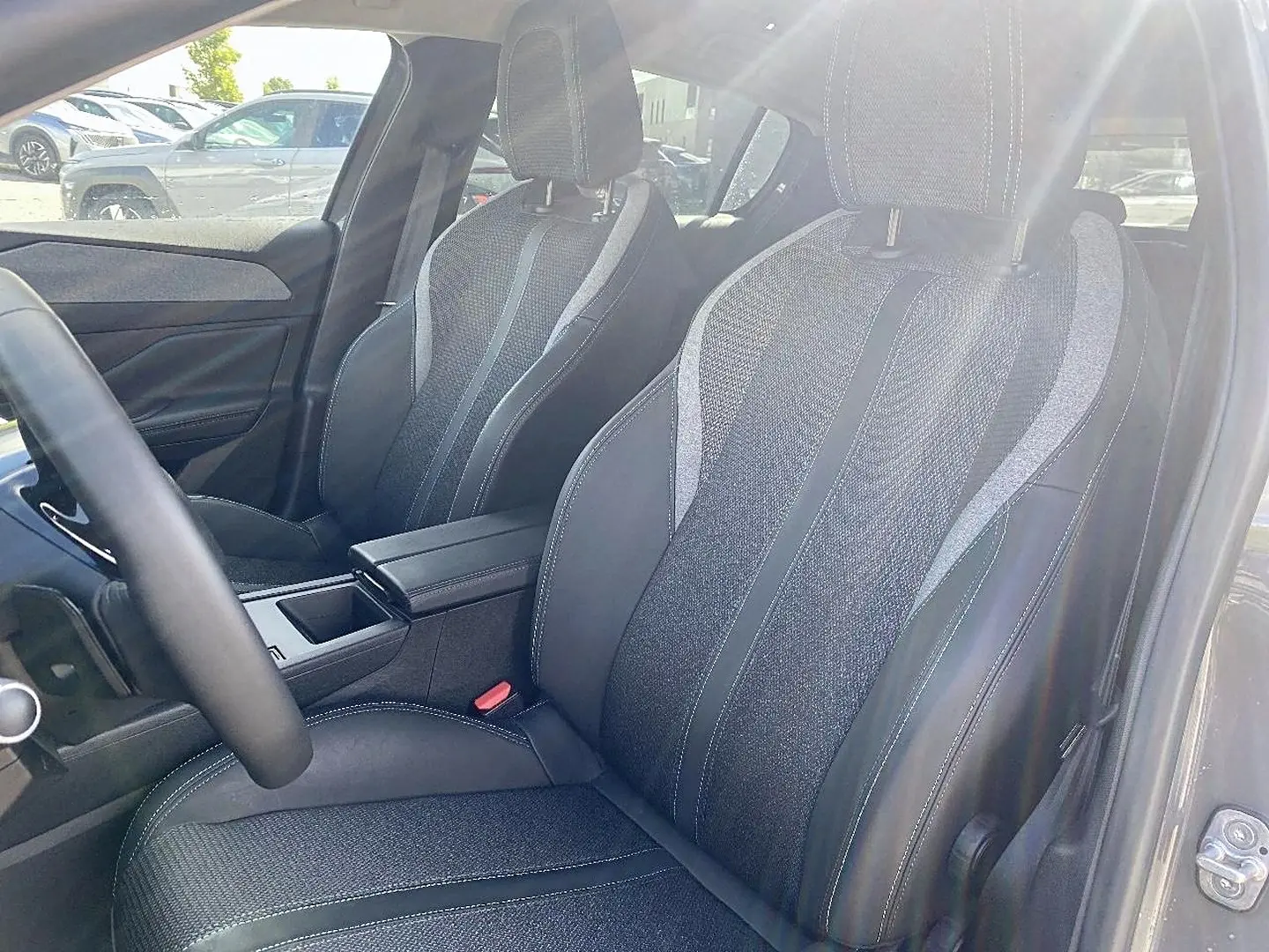 Vue intérieure sur les sièges avant en tissu et cuir noir de la Peugeot 308 gris, avec accoudoir central et volant multifonction.
