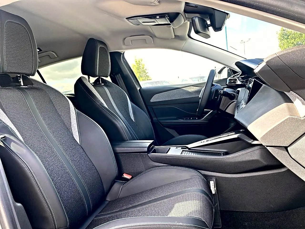 Vue intérieure côté conducteur de la Peugeot 308 2025, sièges noirs avec tissu et cuir, console centrale moderne.