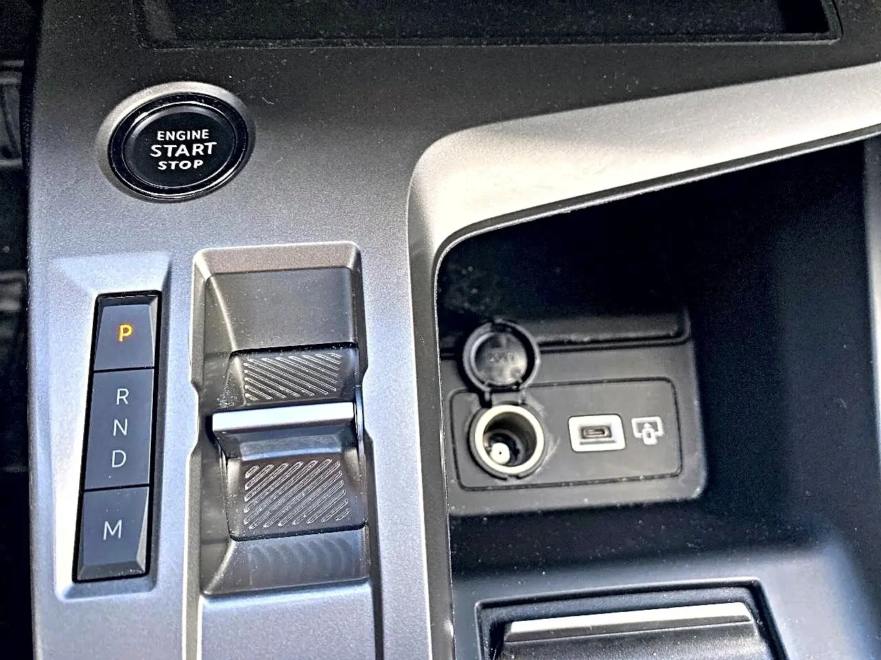 Gros plan sur la console centrale grise de la Peugeot 308 2025 avec bouton start/stop, levier de boîte auto et prises USB/12V.
