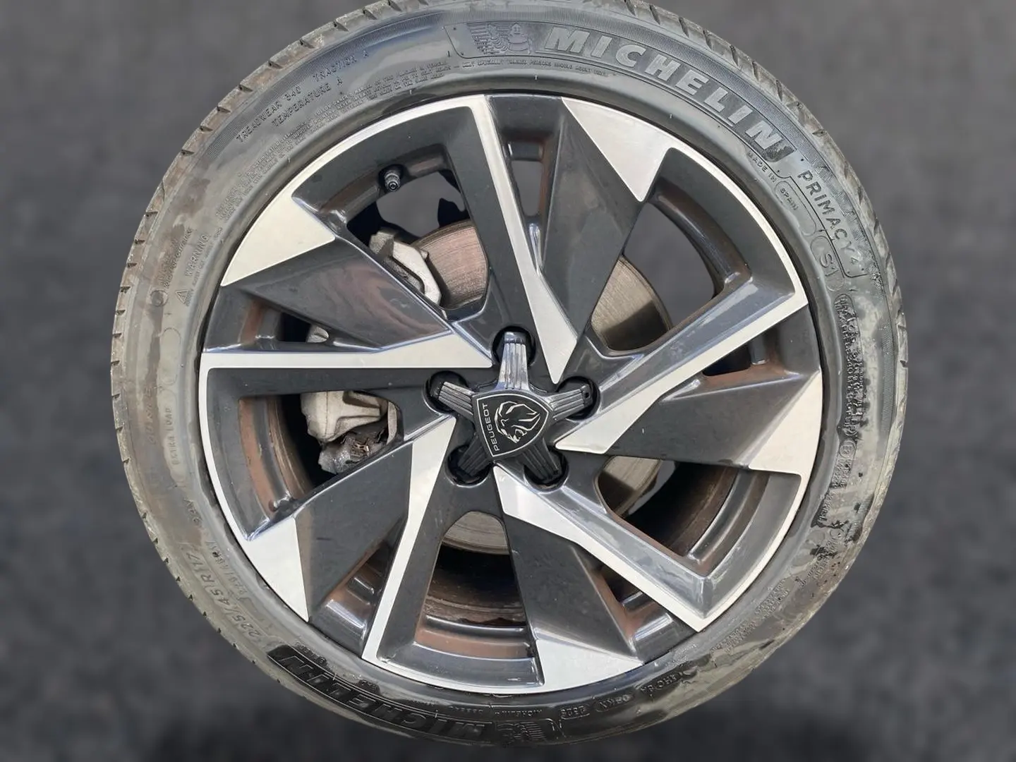 Gros plan sur la jante alu bicolore avec logo Peugeot au centre, montée sur pneu Michelin gris.
