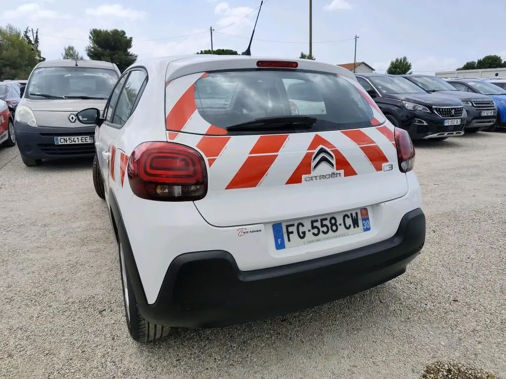 Vue 3/4 arrière droite d'une Citroën C3 Société blanche avec bandes rouges réfléchissantes diagonales sur le hayon.
