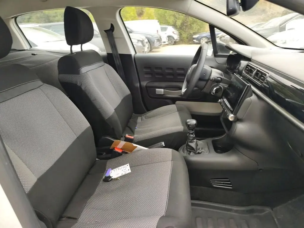 Vue intérieure côté conducteur de la Citroën C3 Société blanche, montrant les sièges tissu gris et la console avec boîte manuelle.