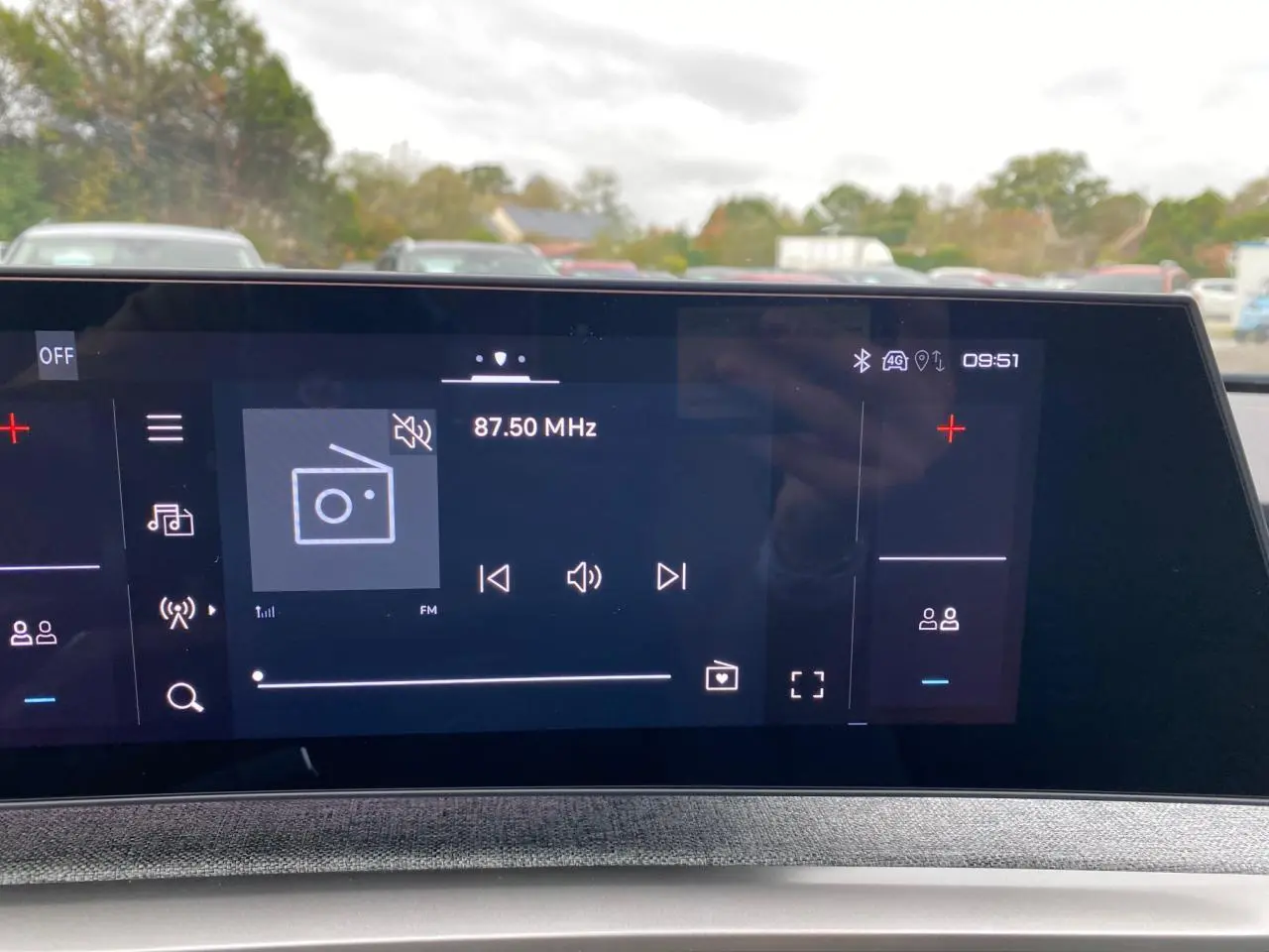 Écran tactile du tableau de bord du Peugeot 3008 Hybrid 2026 affichant la radio FM à 87,50 MHz en extérieur flou.
