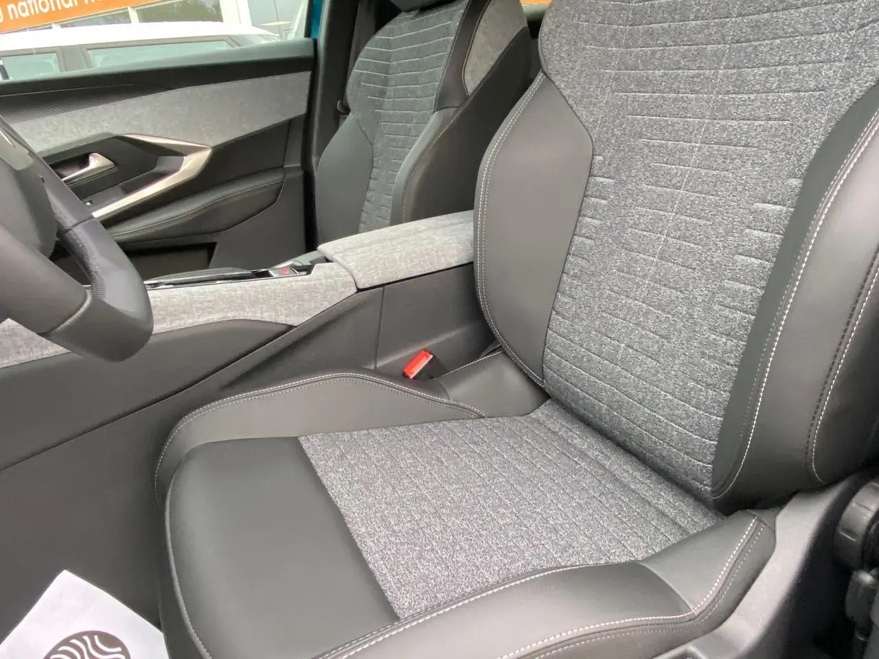 Vue intérieure rapprochée du siège avant droit gris et noir du Peugeot 3008 Hybrid 2026 avec accoudoir central tissu.