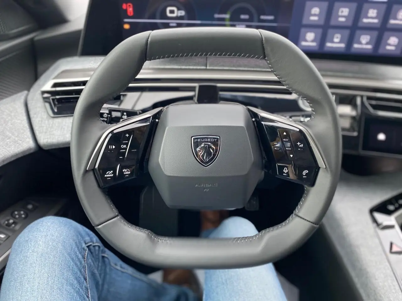Vue rapprochée du volant cuir noir du Peugeot 3008 2026 avec logo lion et commandes intégrées, tableau de bord numérique en arrière-plan.