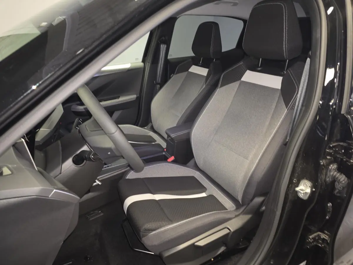 Vue intérieure côté conducteur de l'Opel Frontera-e 2025 noire, sièges tissu bicolore gris et noir avec accoudoir central.