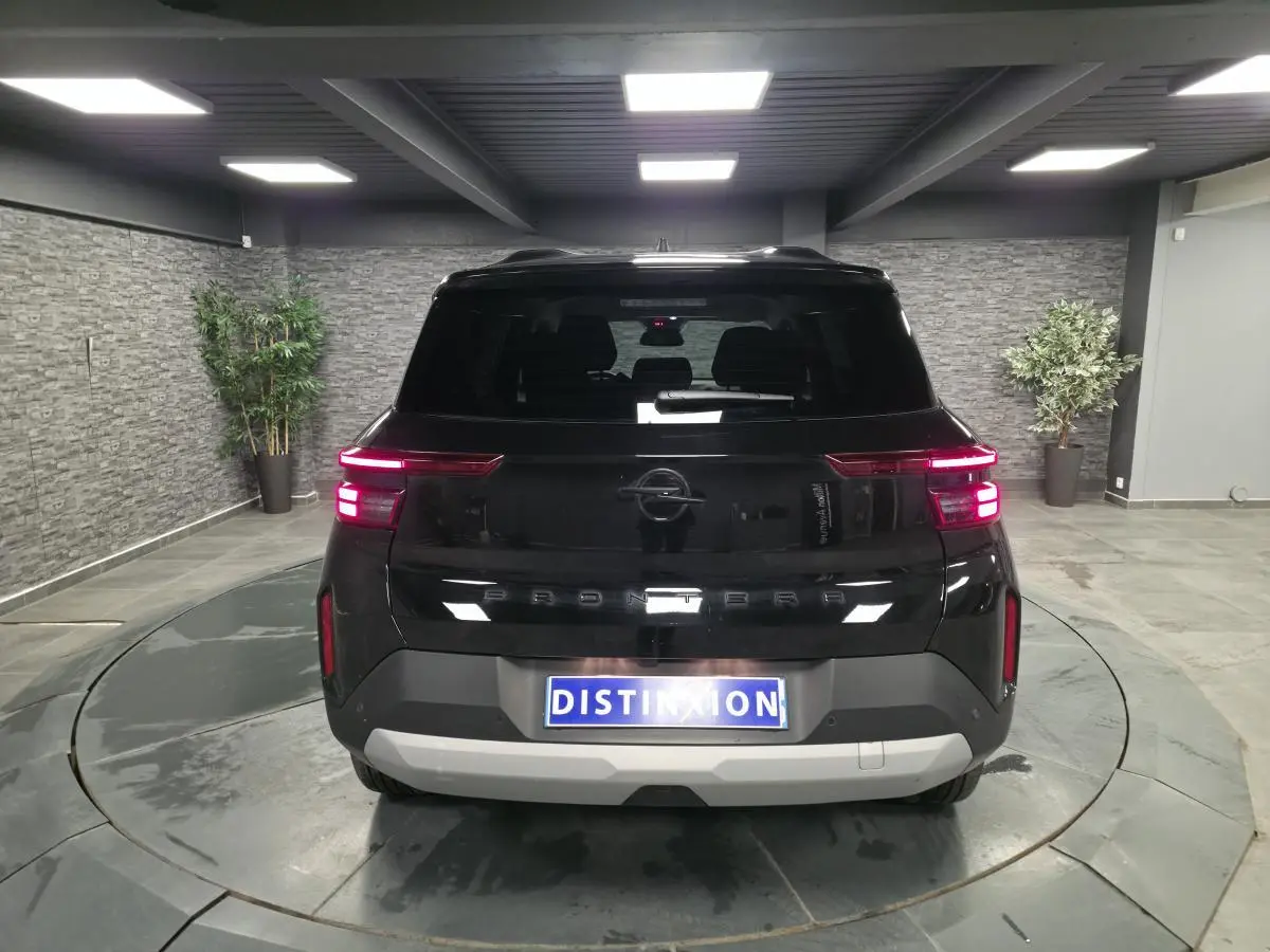 Vue arrière d'un Opel Frontera-e noir métallisé, avec feux LED allumés et logo Opel visible, en intérieur showroom.