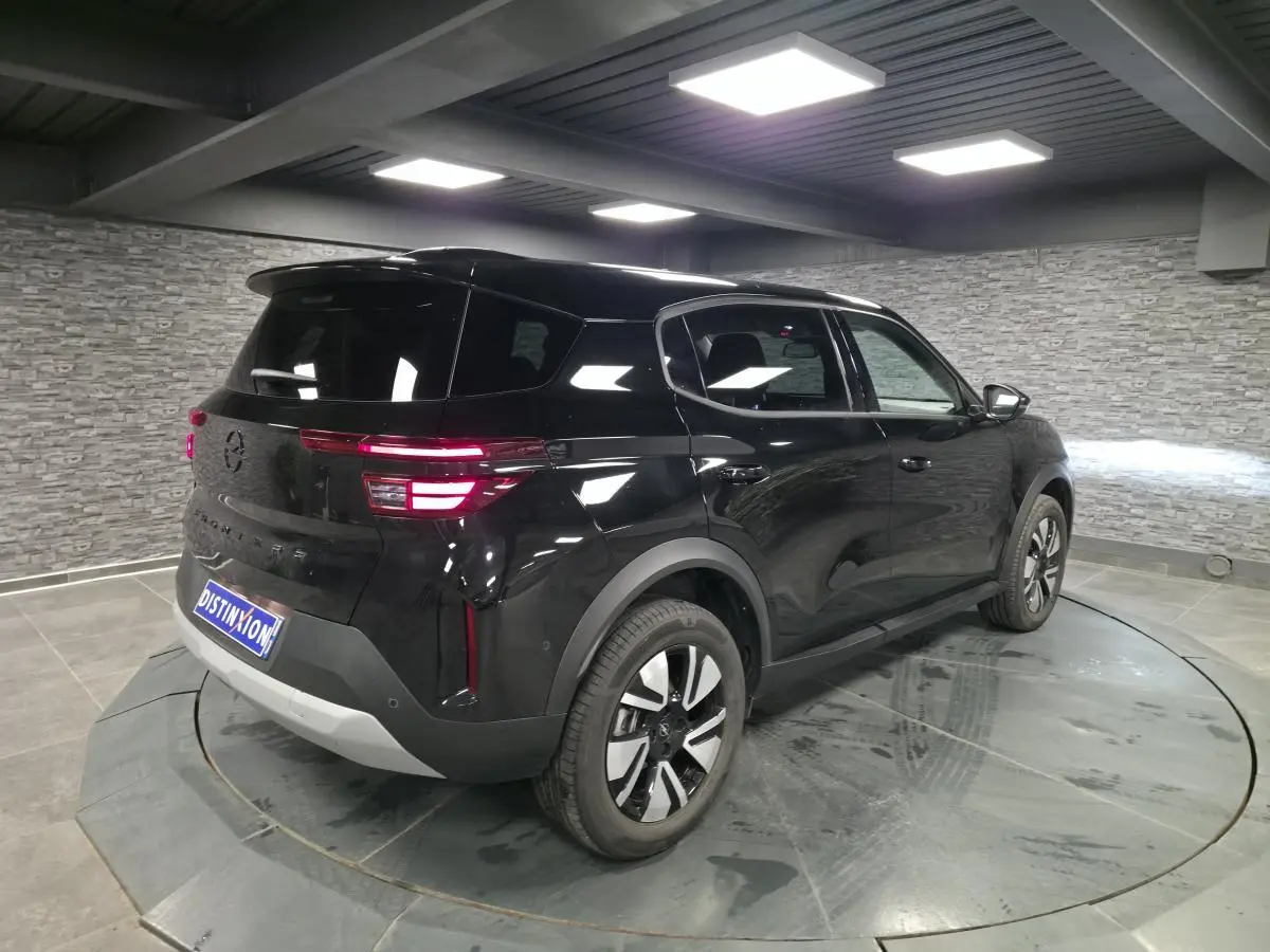 Opel Frontera-e noire vue 3/4 arrière droit, avec jantes alliage 17'' et toit noir Karbon en intérieur showroom.