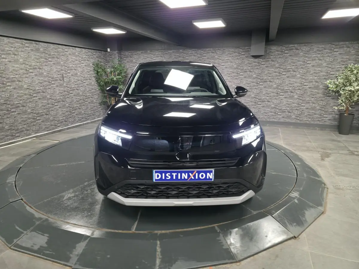 Vue de face d'un Opel Frontera-e noir métallisé avec calandre noire et éclairage LED allumé dans un showroom.