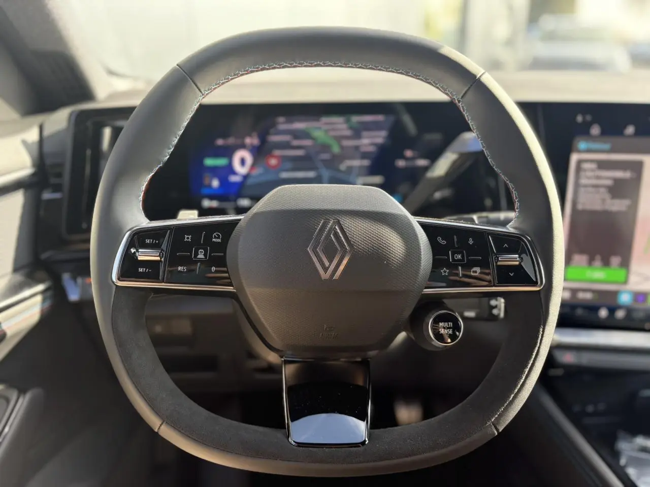 Volant Alcantara avec surpiqûres tricolores et logo Renault, tableau de bord numérique flou en arrière-plan