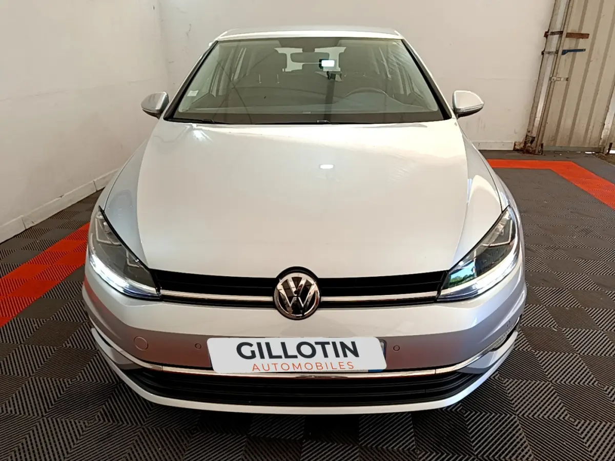 Vue frontale d'une Volkswagen Golf gris clair 2019 avec phares LED allumés dans un garage.