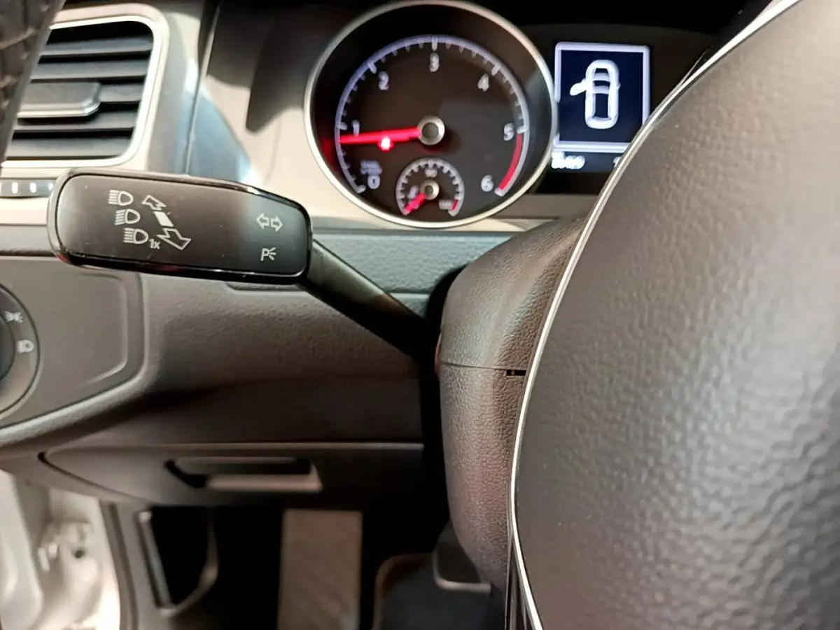 Gros plan sur le volant et le combiné d'instruments du Volkswagen Golf gris clair, avec levier de clignotants visible à gauche.