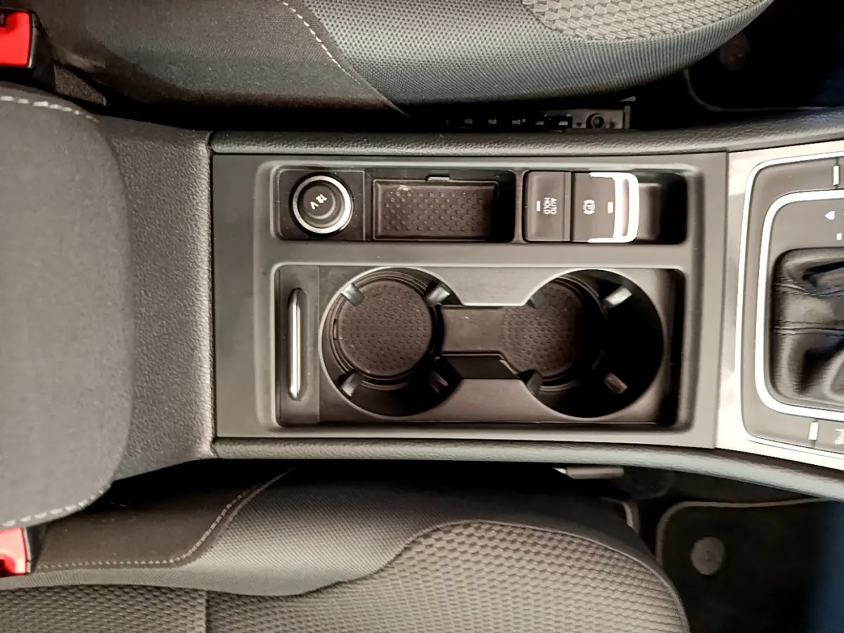 Gros plan sur la console centrale noire de la Volkswagen Golf 1.6 TDI 2019, avec porte-gobelets et bouton frein à main électrique.