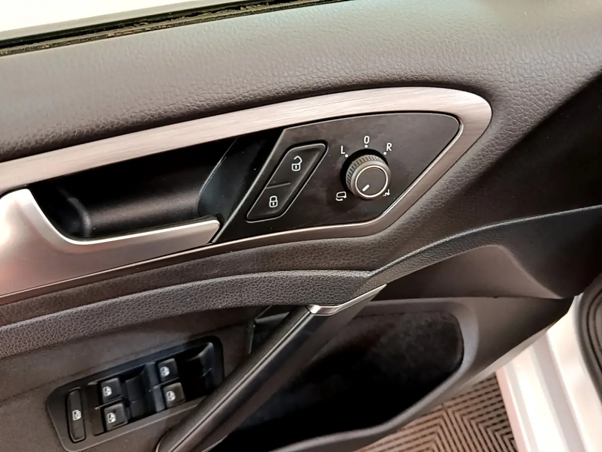 Gros plan sur la porte côté gauche de la Volkswagen Golf gris clair, montrant les commandes des rétroviseurs et des vitres électriques.