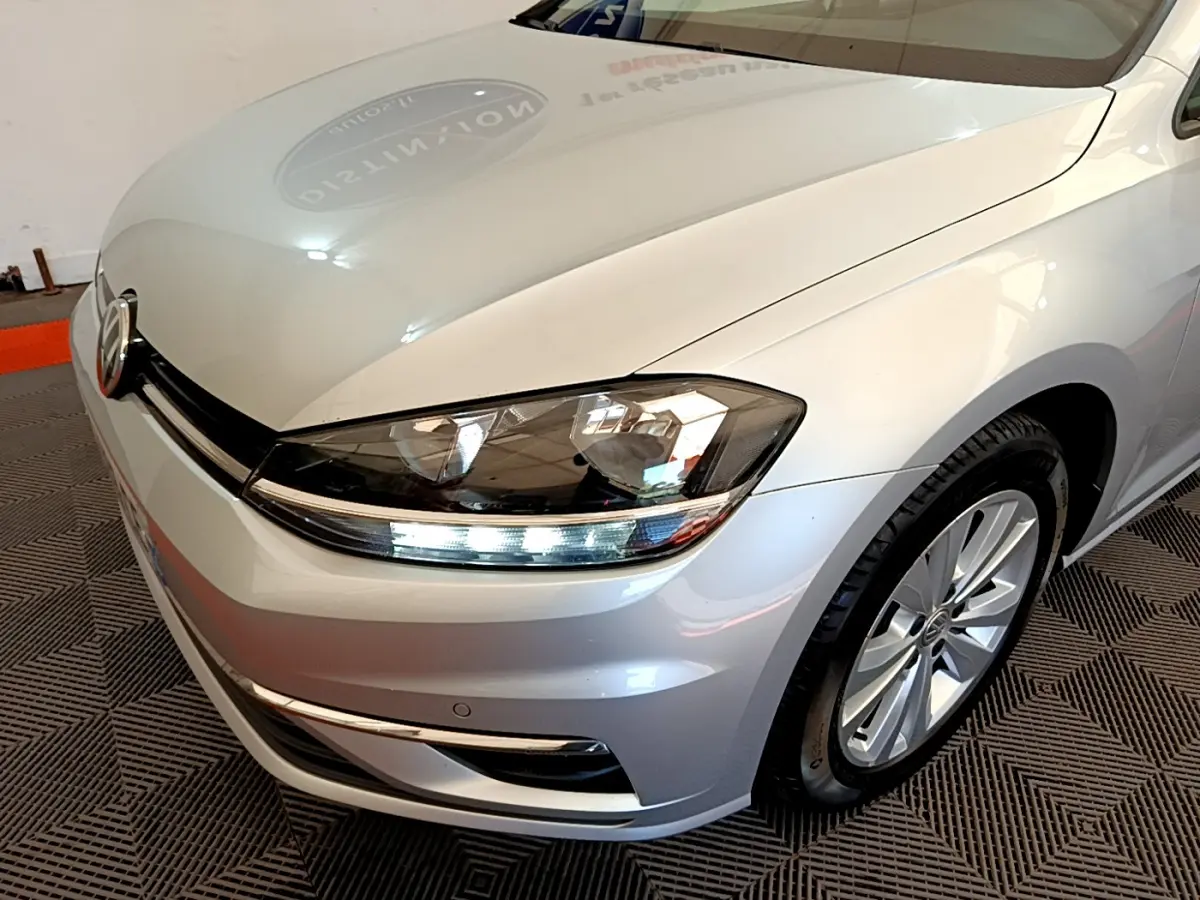 Vue 3/4 avant droit d'une Volkswagen Golf gris clair mettant en valeur le phare LED et la jante alliage.