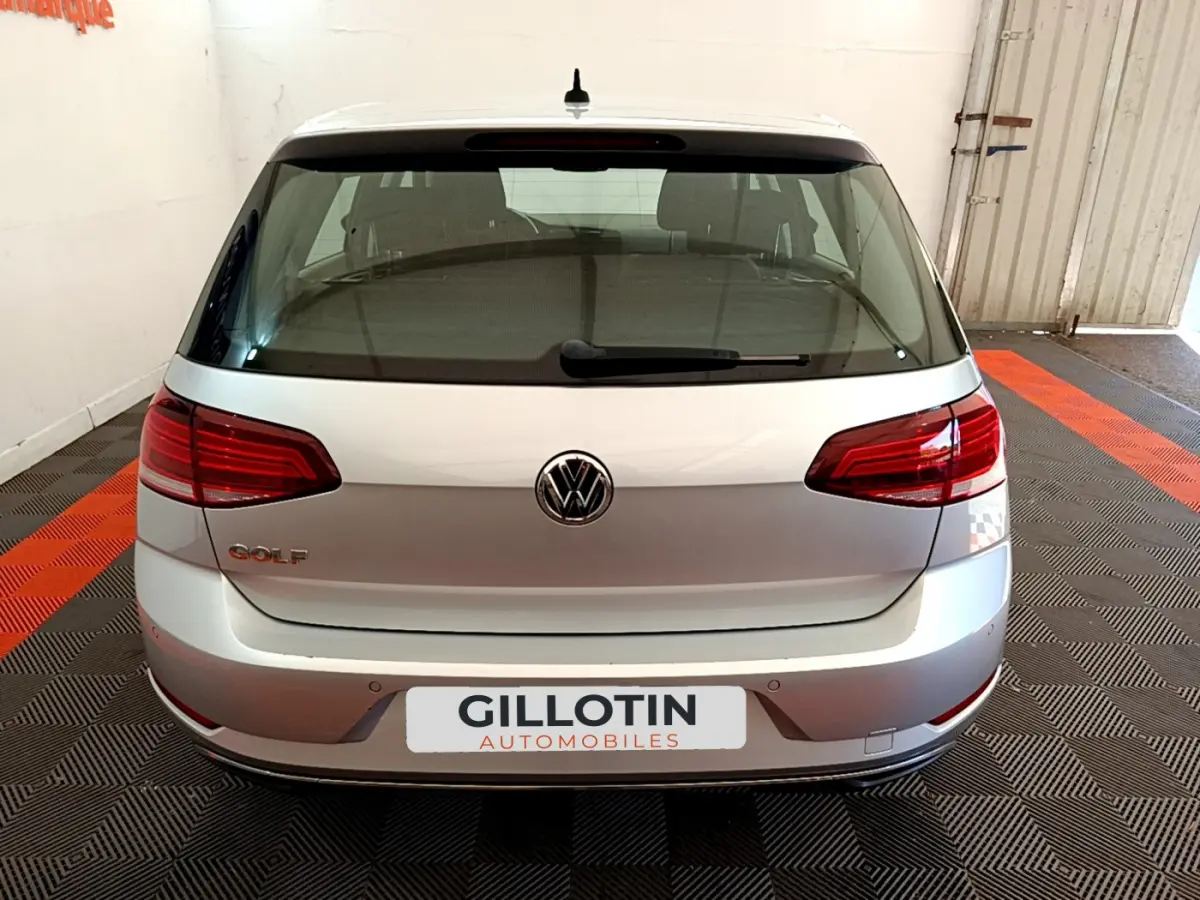 Vue arrière d'une Volkswagen Golf gris clair 2019 garée en intérieur avec logo VW et feux rouges distinctifs.
