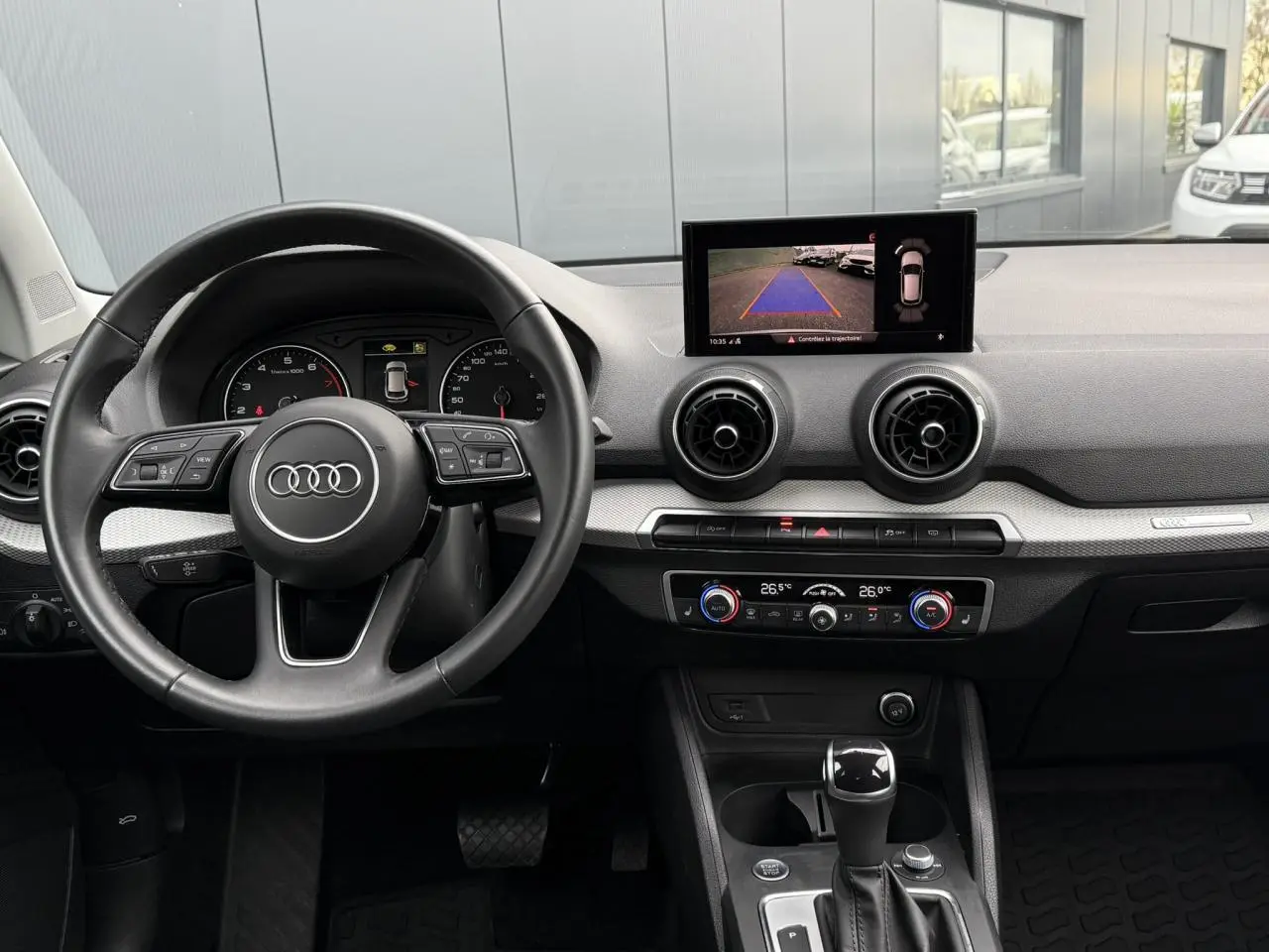 Vue intérieure de l'Audi Q2 35 TFSI 2023 montrant le volant, tableau de bord avec écran caméra de recul et console centrale.