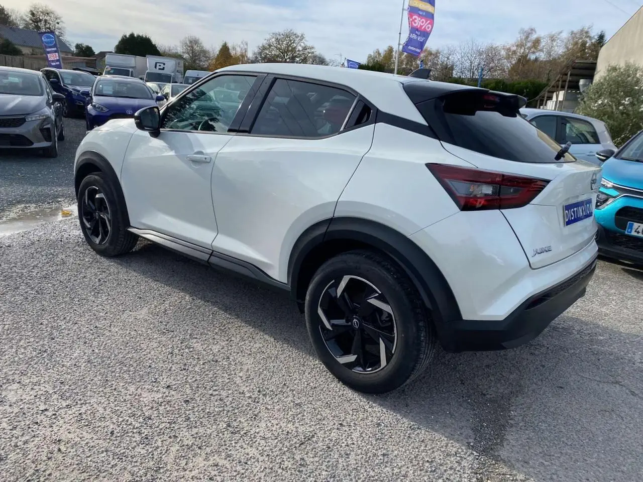 Nissan Juke blanc perle vu en 3/4 arrière droit, avec jantes noires et toit noir contrastant, stationné en extérieur.