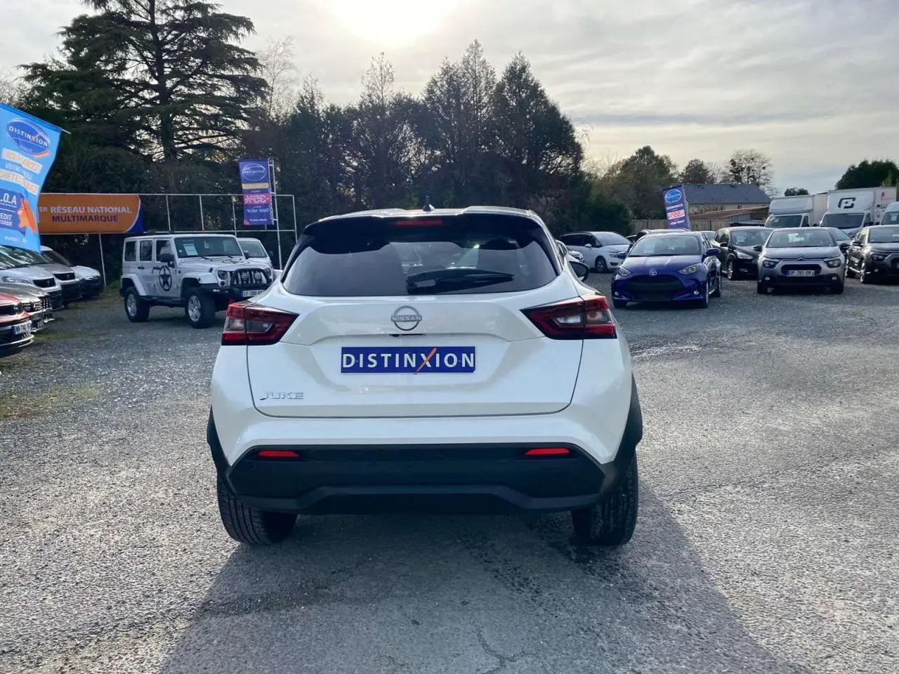Vue arrière d'un Nissan Juke blanc perle 2024 garé sur un parking avec logo Distinxion visible sur le coffre.