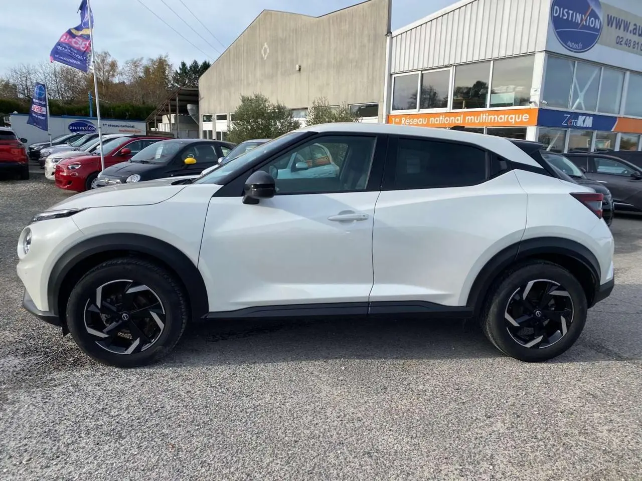 Vue de profil côté gauche d'un Nissan Juke blanc perle 2024 avec jantes noires et détails noirs contrastants.