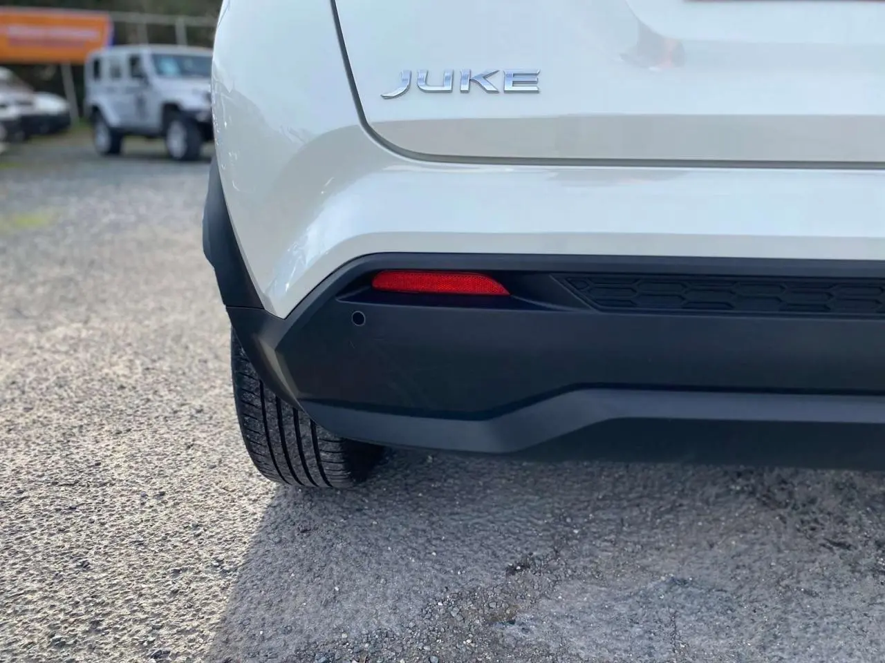 Gros plan sur l'arrière gauche d'un Nissan Juke blanc perle 2024, mettant en valeur le logo et le pare-chocs noir.