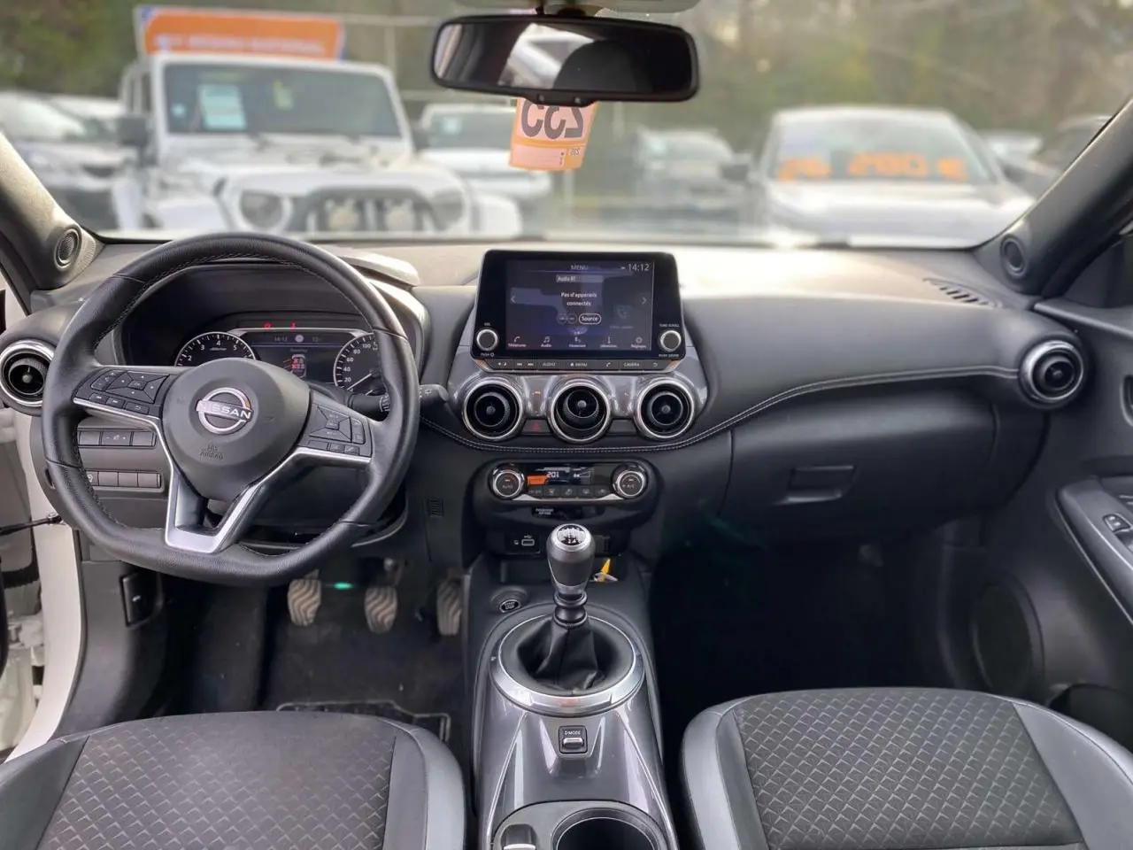 Intérieur du Nissan Juke 2024 blanc perle, vue frontale du tableau de bord avec boîte manuelle et écran tactile central.