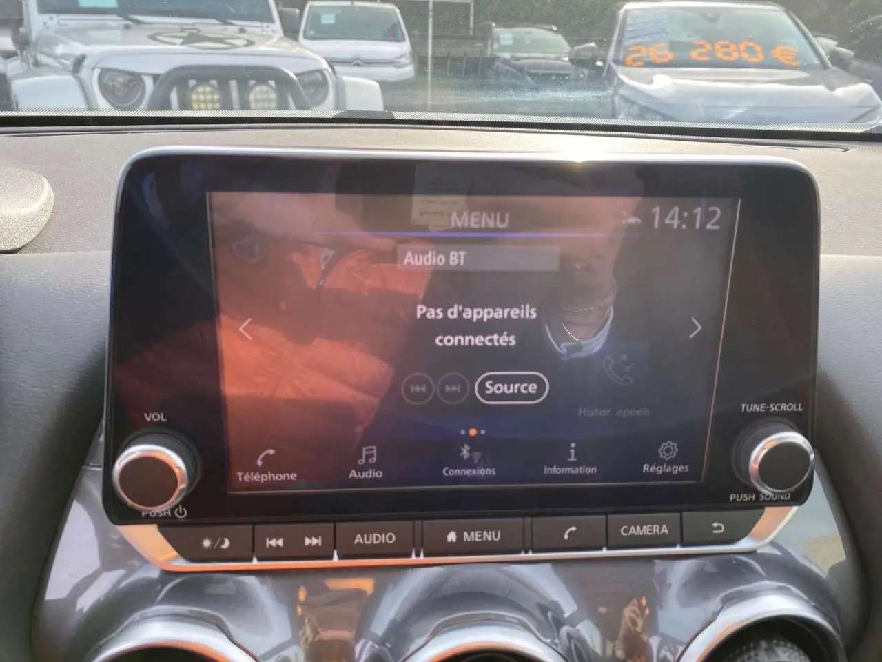 Écran tactile multimédia du Nissan Juke 2024 blanc perle, vue intérieure centrée sur la console avec commandes audio et caméra.