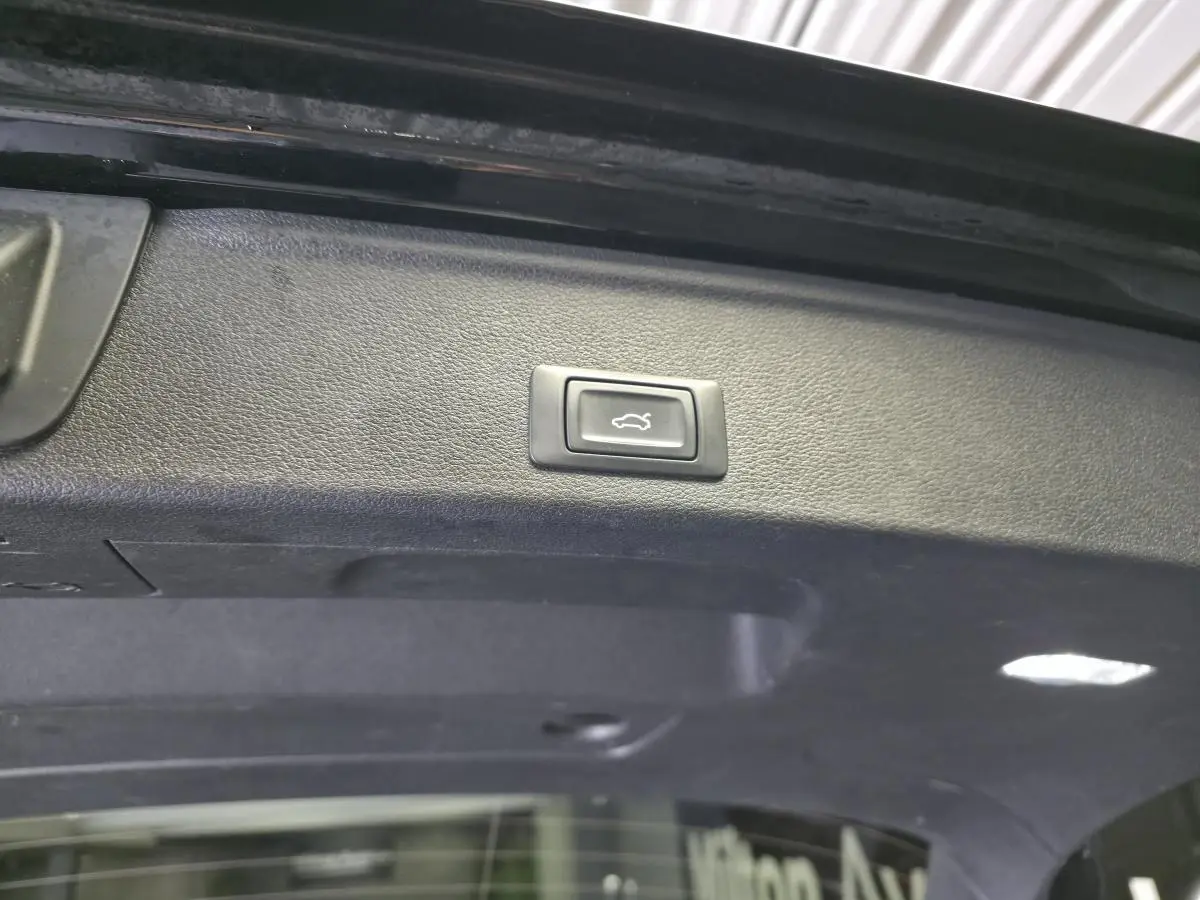 Bouton d'ouverture électrique du coffre sur le hayon intérieur d'une Audi A4 Avant noire, vue rapprochée.