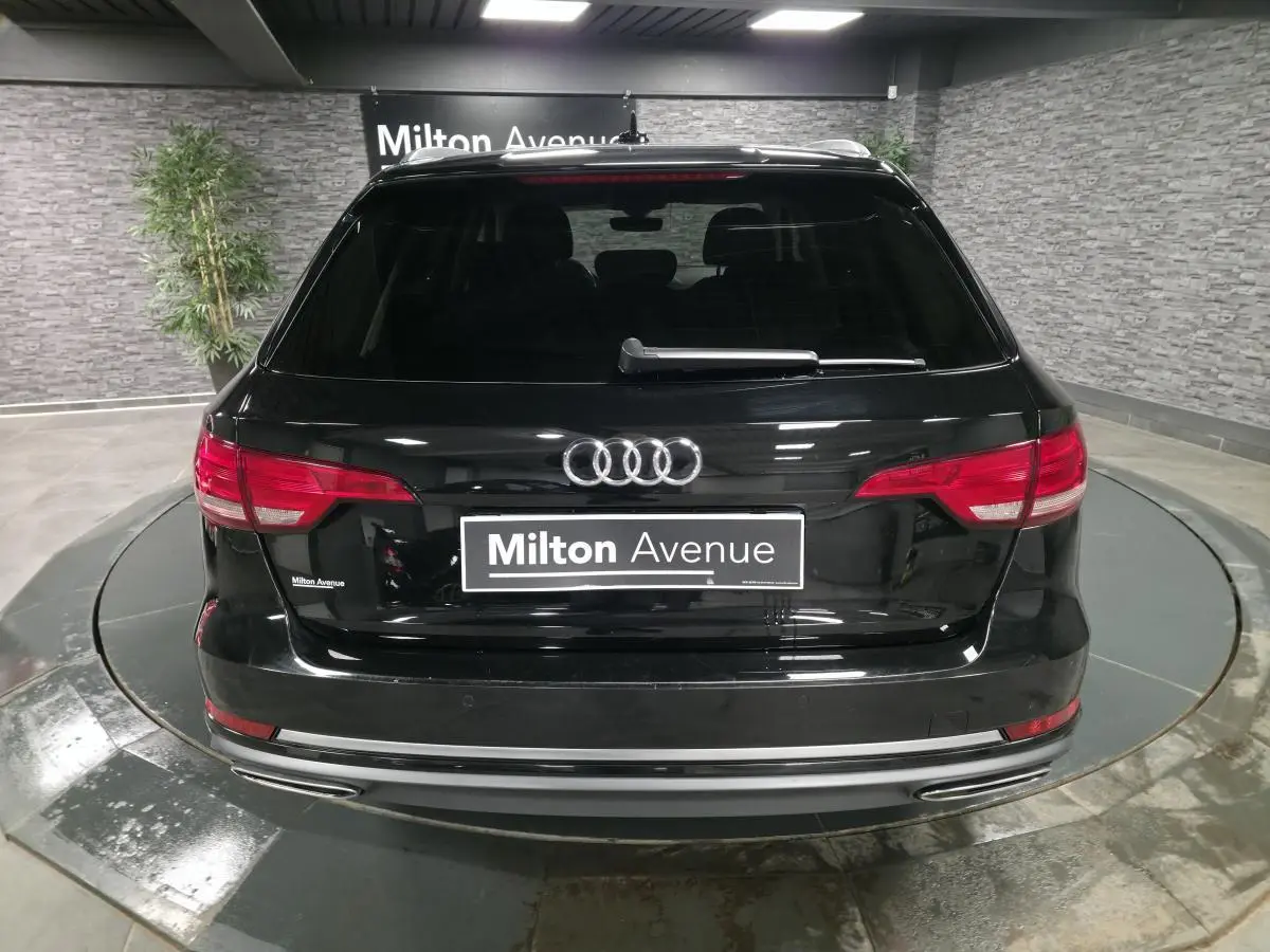 Vue arrière d'une Audi A4 Avant noire avec feux rouges et double sortie d'échappement chromée en intérieur showroom.