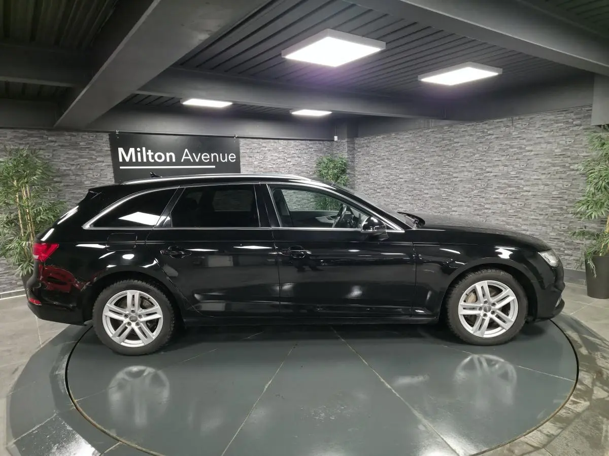 Audi A4 Avant noire vue de profil côté gauche dans un showroom avec jantes aluminium 17 pouces et rétroviseurs noir brillant.