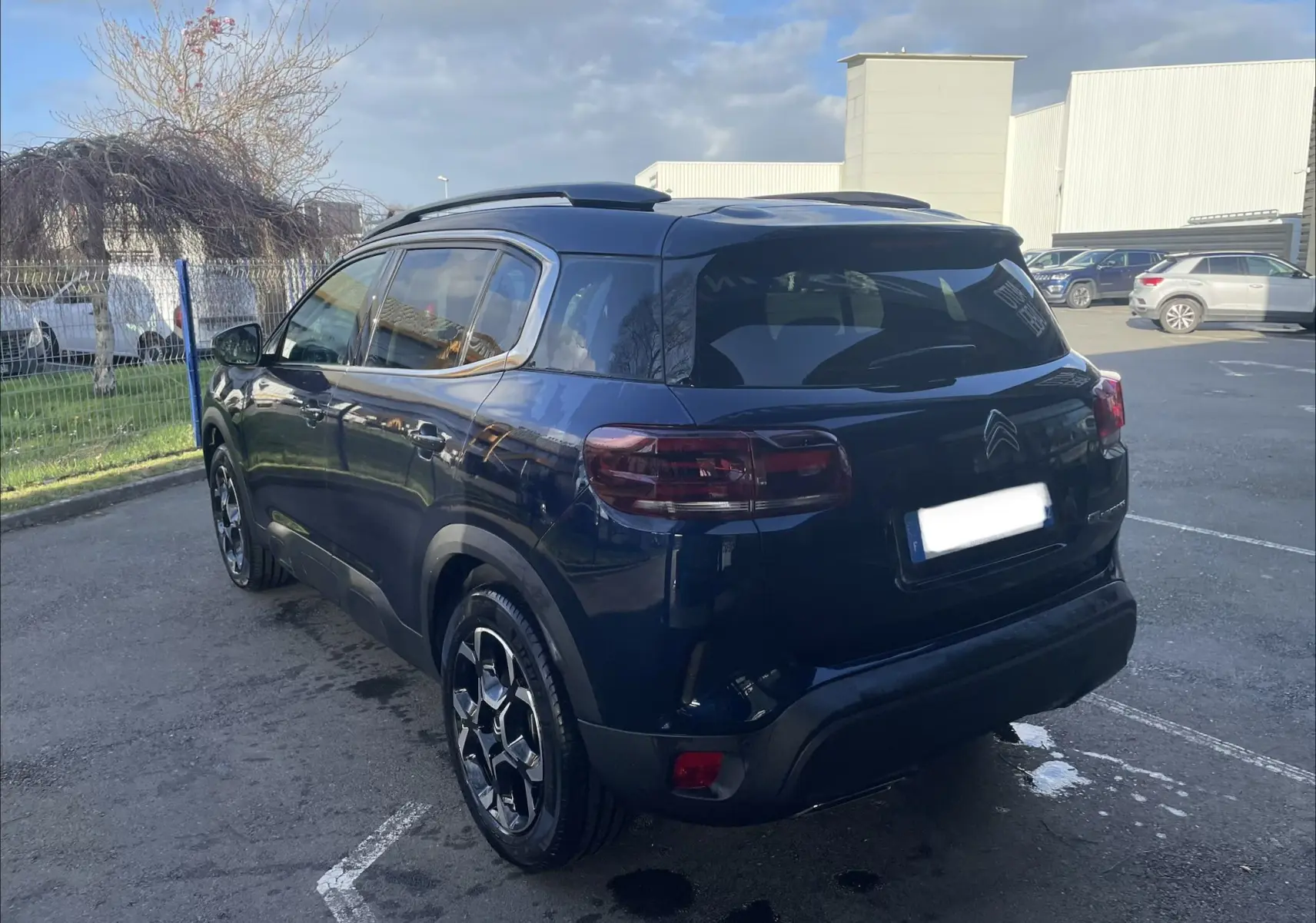 Vue 3/4 arrière droite du Citroën C5 Aircross hybride bleu Eclipse avec jantes alliage biton et barres de toit noires.