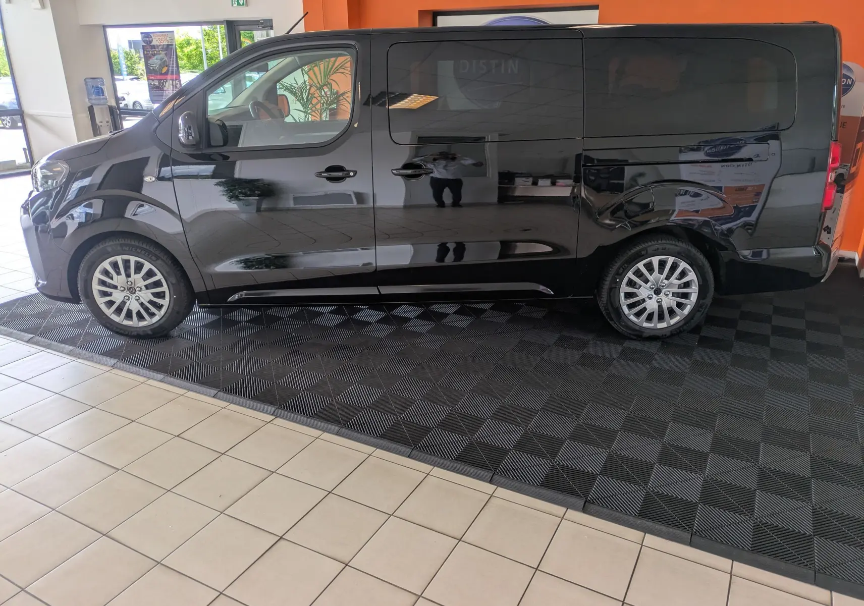 Peugeot Traveller noir vue de profil côté gauche, fourgon spacieux en showroom avec jantes alliage visibles.
