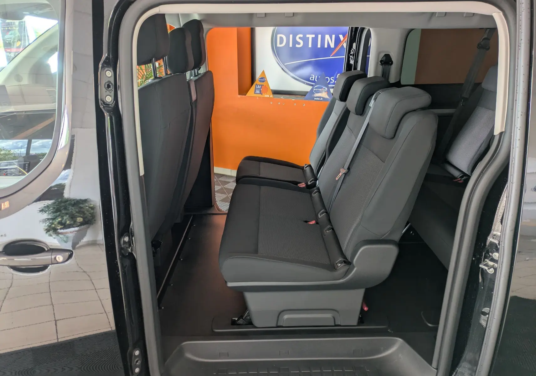 Vue latérale intérieure du Peugeot Traveller noir 2026 montrant les sièges passagers en tissu et la porte coulissante ouverte.