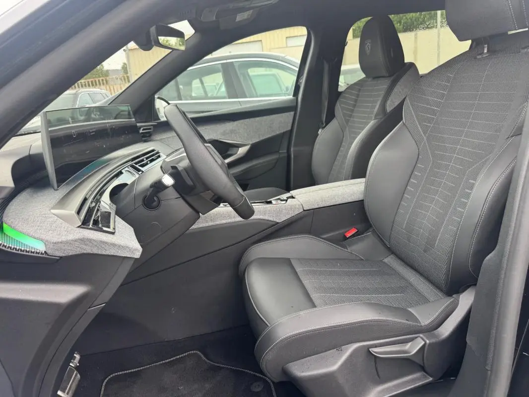 Vue intérieure côté conducteur du Peugeot 5008 Hybrid 145 ch GT 2025, sièges noirs avec accoudoir central et tableau de bord numérique.