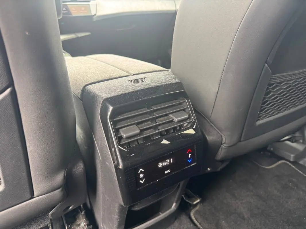 Vue rapprochée de la console centrale arrière du Peugeot 5008 noir, avec commandes climatisation digitale et sièges en cuir gris.