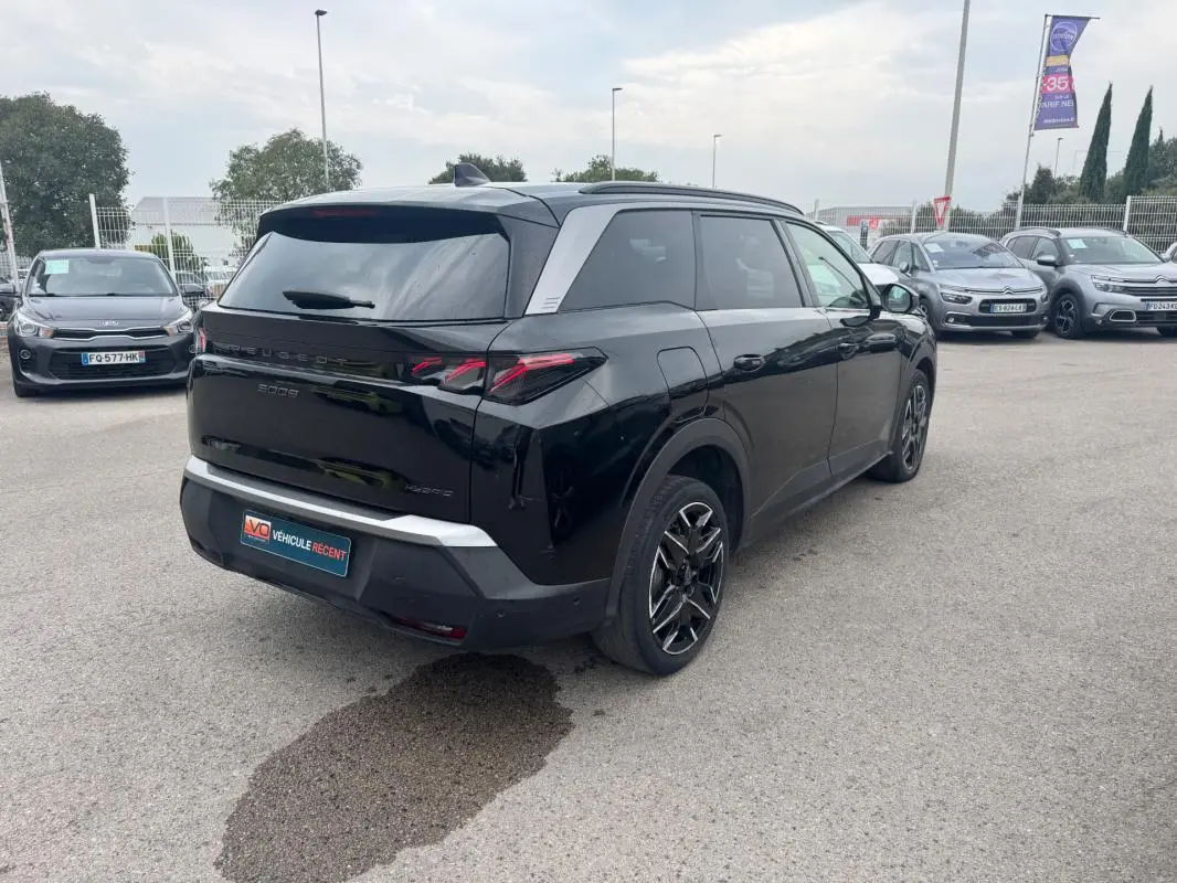 Vue 3/4 arrière droite d'un Peugeot 5008 noir 2025 avec jantes alliage 19 pouces et barres de toit visibles.