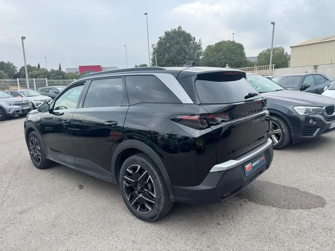 Peugeot 5008 Hybrid noir vue 3/4 arrière droit, avec jantes alliage noires et barres de toit visibles.