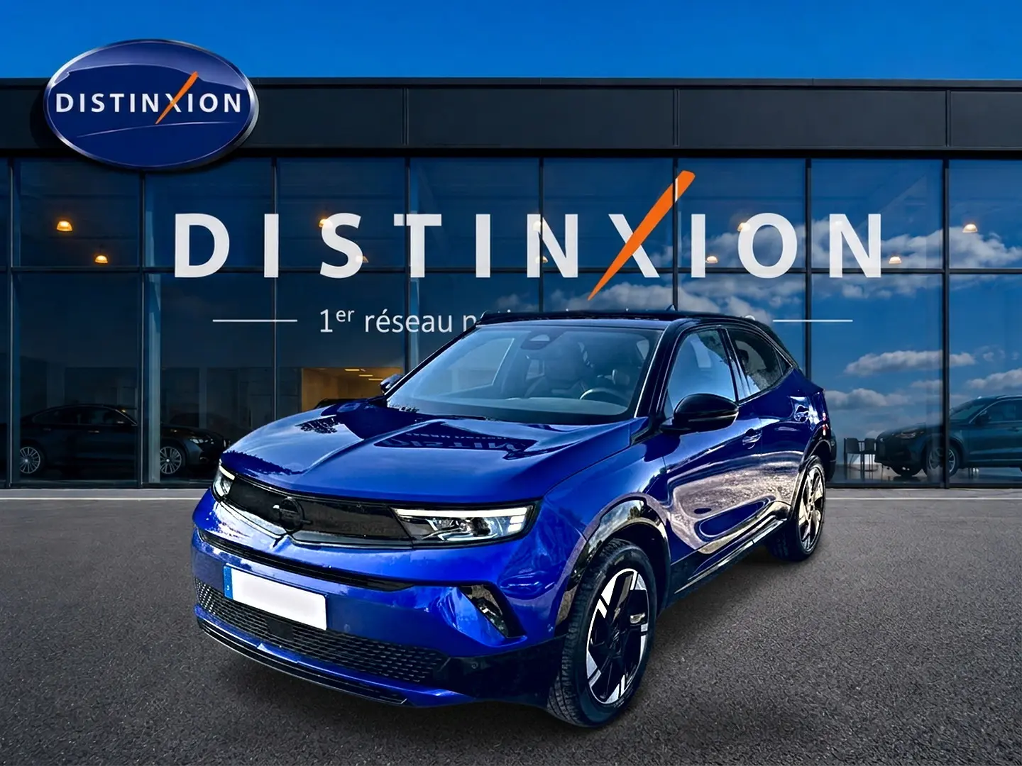 Opel Mokka Electric 156 gs bleu en 3/4 avant droit devant une vitrine avec logo Distinxion.