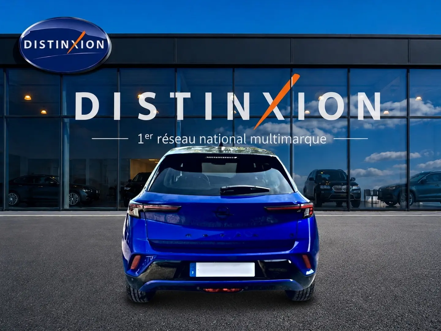 Vue arrière d'un Opel Mokka Electric 156 gs bleu, garé devant une vitrine avec logo Distinxion.