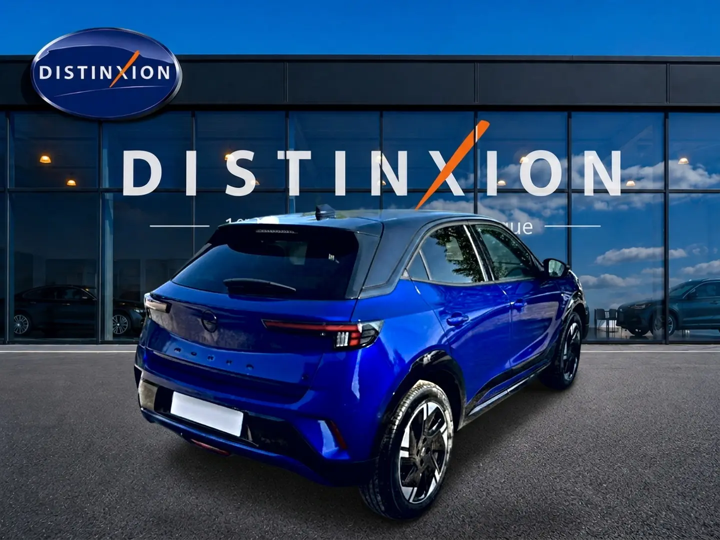 Vue 3/4 arrière droite d’un Opel Mokka Electric 156 gs bleu avec toit noir devant une vitrine Distinxion.