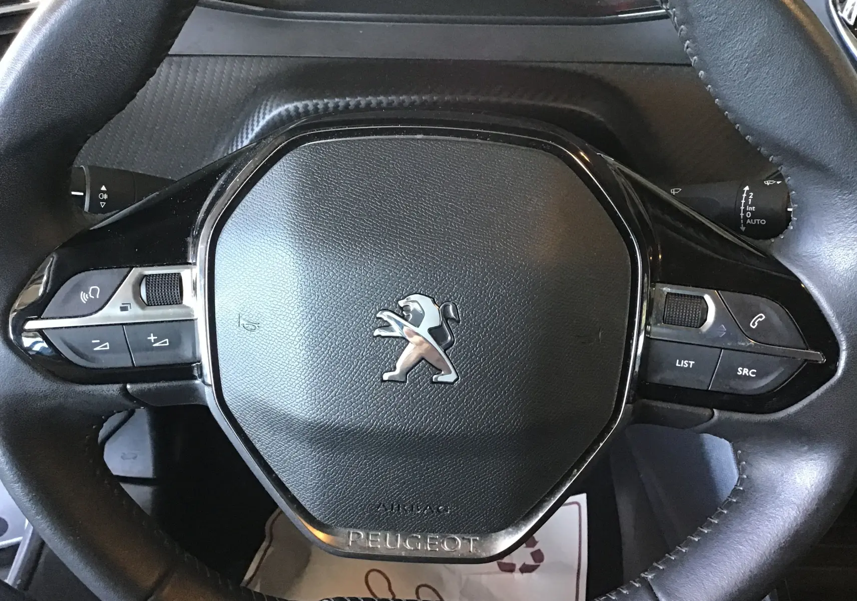Gros plan sur le volant cuir noir du Peugeot 2008 1.5 BlueHDi 110, avec commandes intégrées et logo lion central.
