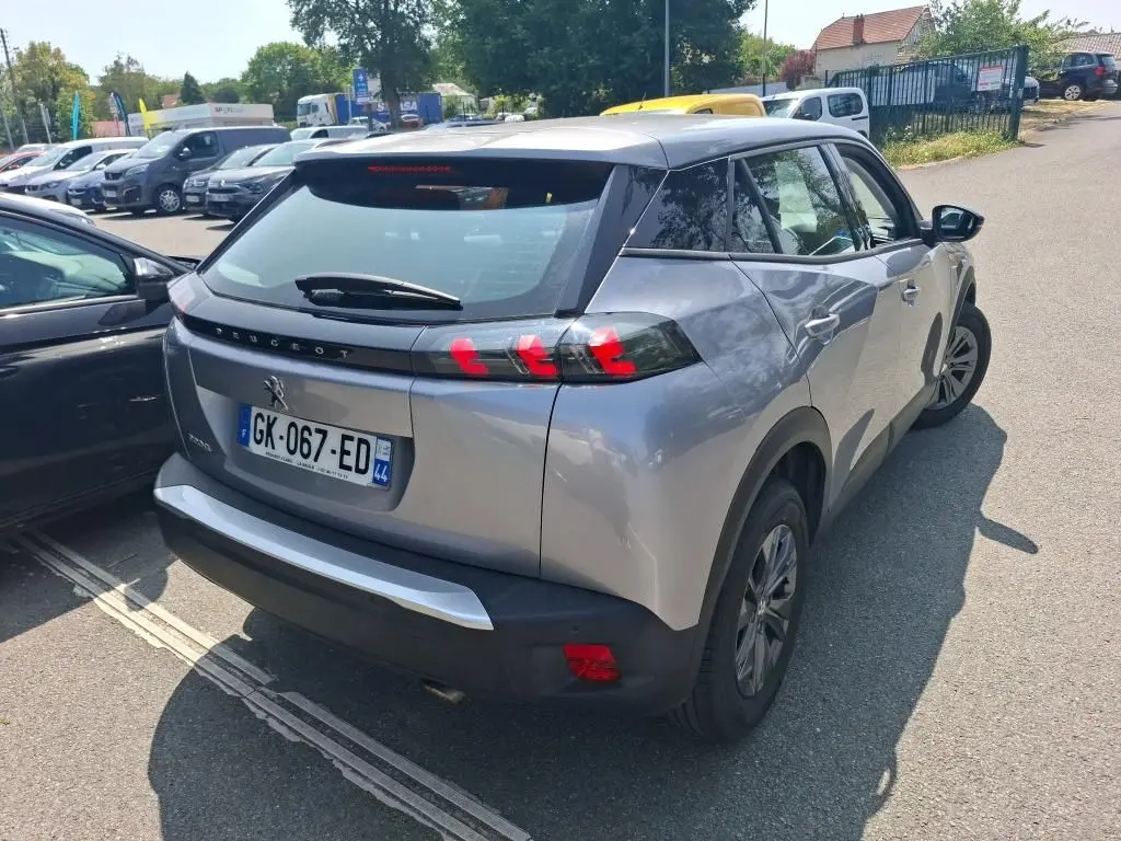Peugeot 2008 gris Artense vue de profil côté gauche sur parking gravillonné avec protections noires sur les passages de roues.