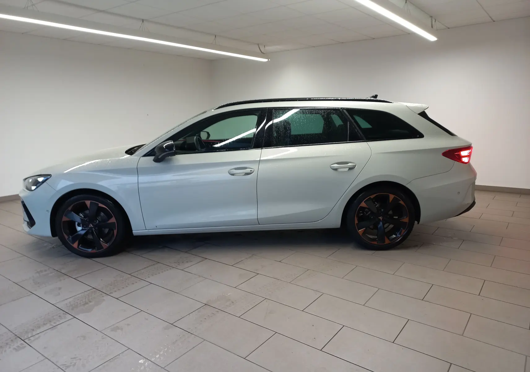 Vue de profil côté gauche d'une CUPRA LEON ST 1.5 eTSI 150 DSG7 gris Taiga avec jantes alliage 18'' cuivrées.