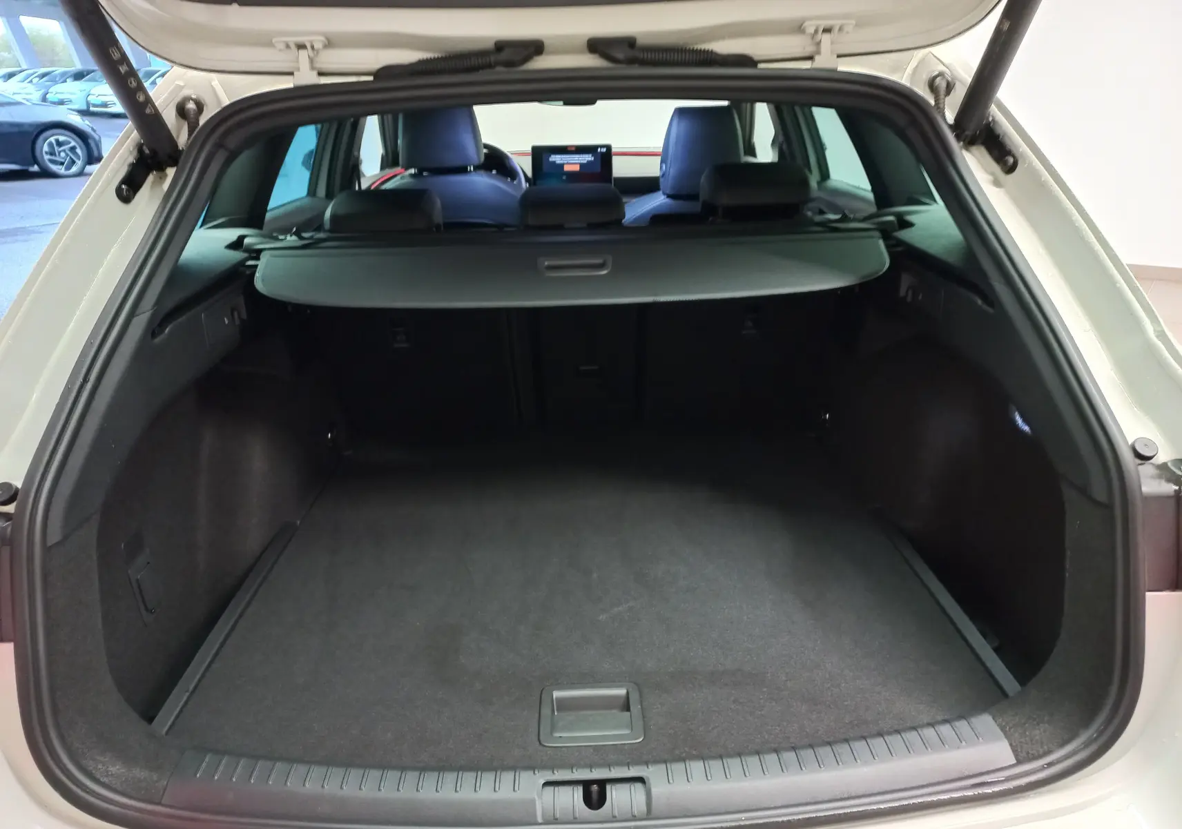 Coffre ouvert vu de l’arrière d’une CUPRA LEON ST 1.5 eTSI gris Taiga avec cache-bagages et intérieur noir.