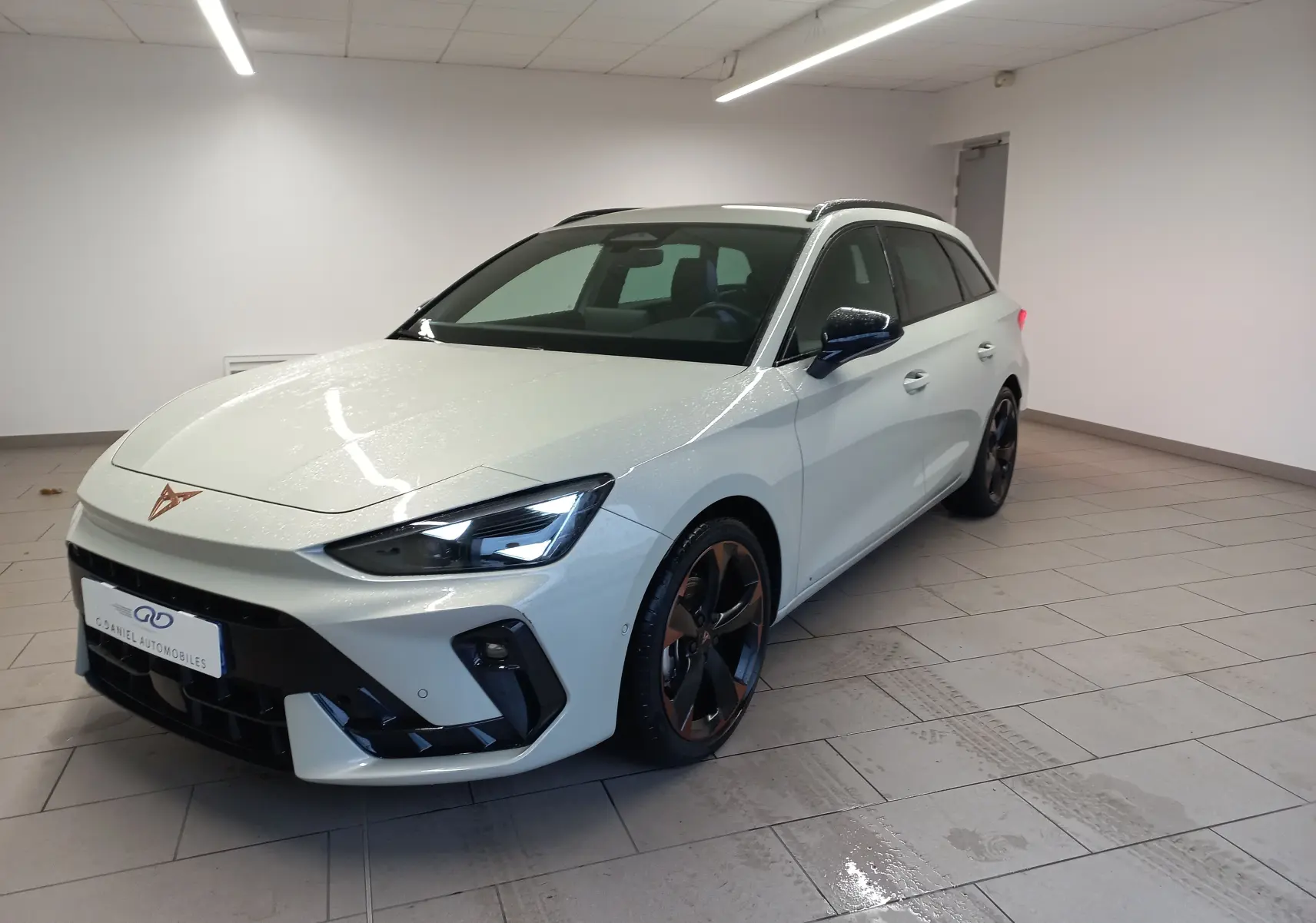 Vue 3/4 avant droite d'une CUPRA Leon ST gris Taiga avec jantes alliage 18'' cuivrées dans un showroom.